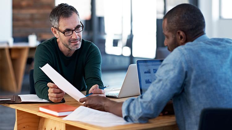 Two men talking about small business benefits and working on a laptop.